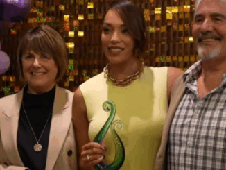 Mila Reuelu-Buchanan holding a green glass award, standing between two supporters at the Stars Awards Night in Karaka. Ask ChatGPT