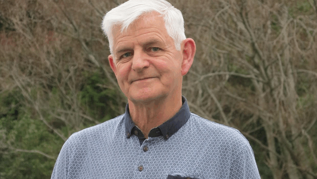 Porirua City Councillor Mike Duncan standing outdoors, smiling, with native bush in the background.