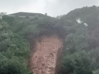 Muddy landslip debris piled against the rear walls of suburban houses in Porirua, with emergency cones and tape visible nearby.