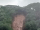 Muddy landslip debris piled against the rear walls of suburban houses in Porirua, with emergency cones and tape visible nearby.
