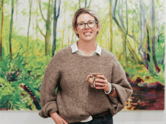 Alicja Gear, art tutor, standing in front of a colourful painting holding a cup.