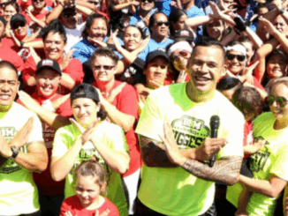 Dave Letele leads a large crowd wearing BBM shirts and making an X with their arms during a community event.