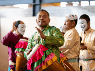 A group of men in traditional Southeast Asian attire perform with colourful drums and masks during a cultural celebration.