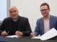 Helmut Modlik and Nigel Corry seated at a table signing documents during the lease agreement ceremony between Ngāti Toa Rangatira and Greater Wellington.