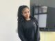 Teenage girl in black Nike sweatshirt, smiling and standing indoors.