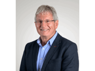 Ross Leggett wearing glasses, a blue shirt, and a dark blazer, smiling against a plain light background.