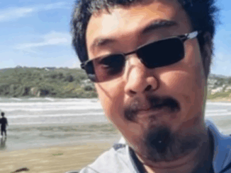 Jinting Guo wearing sunglasses and looking at the camera with a beach and ocean in the background