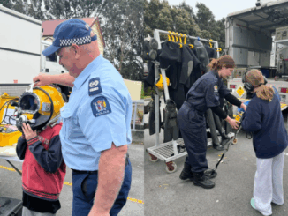 Two children interacting with New Zealand Police Dive Squad officers and trying on diving equipment during a holiday event.