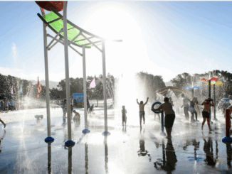 Kids playing among colourful water fountains and splash buckets at Aotea Lagoon’s water play area in Porirua on a bright summer day.