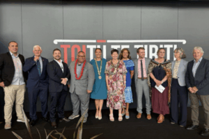 Group photo of Porirua City Council members standing in a row in front of a wall with the words "Toitū Te Tiriti." Mayor Anita Baker is at the centre wearing the mayoral chain, surrounded by councillors dressed in formal attire.