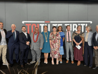 Group photo of Porirua City Council members standing in a row in front of a wall with the words "Toitū Te Tiriti." Mayor Anita Baker is at the centre wearing the mayoral chain, surrounded by councillors dressed in formal attire.