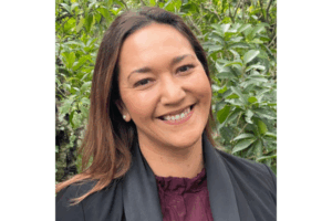 Portrait of Kylie Wihapi smiling outdoors with greenery in the background.