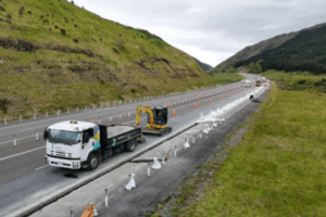 Roadworks underway on State Highway 1 Transmission Gully, with trucks, excavators, and traffic cones visible.