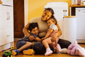 Mother hugs her two young children on the floor of a warm family home in Porirua.