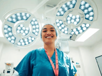 Doctor in surgical scrubs smiles beneath operating theatre lights.