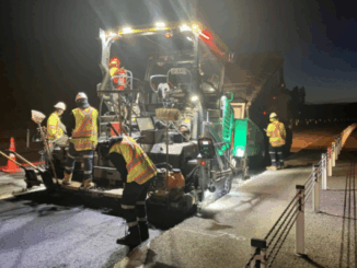 Night-time roadworks underway on Transmission Gully, with workers operating paving machinery under floodlights while traffic lanes are closed.