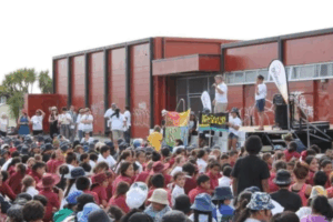A large group of children and young people sit outdoors facing a stage during a community event hosted by Wesley Community Action.