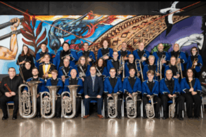 Members of Porirua City Brass pose for a formal group photo, wearing blue jackets and holding brass instruments.