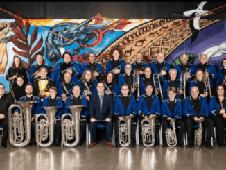 Members of Porirua City Brass pose for a formal group photo, wearing blue jackets and holding brass instruments.
