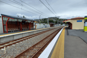 Plimmerton railway station platforms with empty tracks, shelters and overhead power lines on a cloudy day.