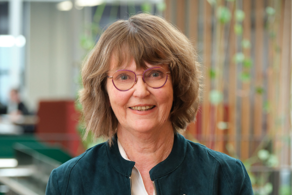 Adrienne Staples is pictured indoors, wearing glasses and a dark jacket, with a softly blurred background. She is smiling in a professional portrait taken during her time in public office.