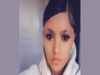 Portrait of a young teenage girl with black hair parted in the middle and styled back, wearing a light-coloured hoodie, looking directly at the camera with a neutral expression.