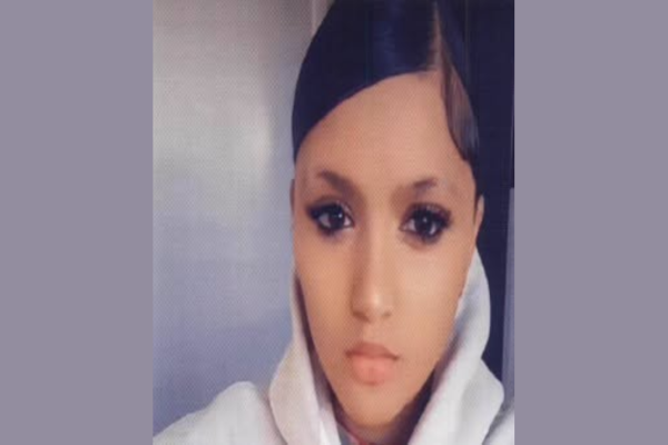 Portrait of a young teenage girl with black hair parted in the middle and styled back, wearing a light-coloured hoodie, looking directly at the camera with a neutral expression.