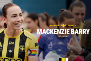 Mackenzie Barry smiles in a Wellington Phoenix kit while standing among teammates, with a club graphic announcing her re-signing overlaid on the image.