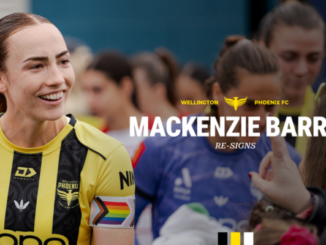 Mackenzie Barry smiles in a Wellington Phoenix kit while standing among teammates, with a club graphic announcing her re-signing overlaid on the image.