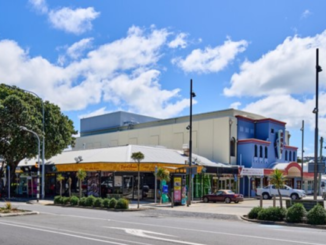 A corner commercial building in Miramar with a white façade and yellow signage, set along a wide street under a blue sky with scattered clouds.