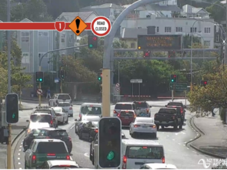 Busy Wellington intersection with multiple lanes of traffic waiting at lights, overhead signage warning of road closures ahead.