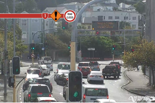 Busy Wellington intersection with multiple lanes of traffic waiting at lights, overhead signage warning of road closures ahead.