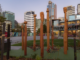 Tall carved wooden tumu sculptures stand in Te Ngākau Civic Square, with modern city buildings rising in the background.