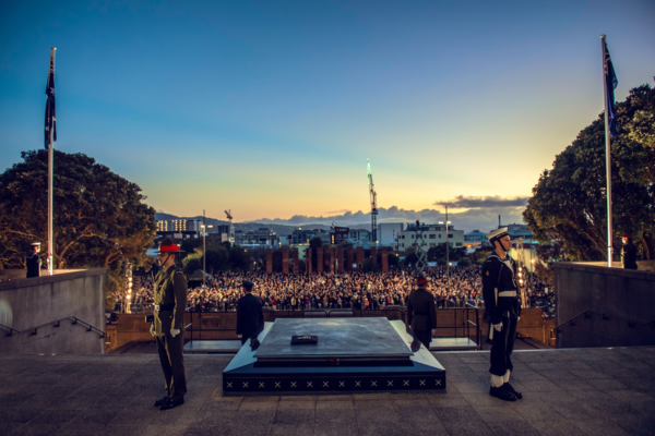 Uniformed service personnel stand guard beside a cenotaph at dawn, overlooking a large crowd gathered for an Anzac Day service in Wellington.