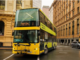 A yellow double-decker Metlink bus drives through a city street lined with historic buildings on a wet day.