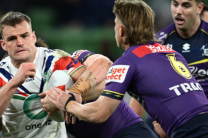 A Warriors player holds the ball while being tackled by two Dolphins players during an NRL match.