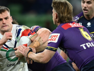 A Warriors player holds the ball while being tackled by two Dolphins players during an NRL match.
