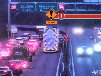 Traffic is backed up on a motorway as emergency services respond to a crash, with warning signage visible above the road.