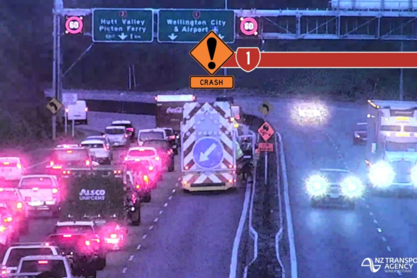 Traffic is backed up on a motorway as emergency services respond to a crash, with warning signage visible above the road.