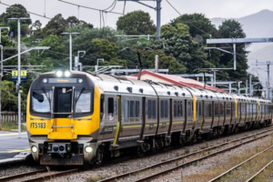 A yellow and silver Metlink train travels along railway tracks beside a Wellington station platform.