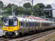 A yellow and silver Metlink train travels along railway tracks beside a Wellington station platform.