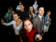 Promotional image for Waenga showing eight cast members against a black background. A young woman wearing a red scarf stands in the foreground holding an identification card, while other characters, including police officers, a lawyer and young adults, look towards the camera.