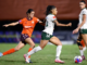 Wellington Phoenix player dribbles forward with the ball while a Brisbane Roar opponent chases closely behind during a semi-final match.