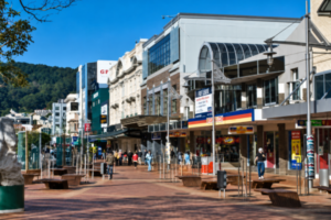 People walk along Courtenay Place in central Wellington, with shops, businesses and outdoor seating lining the street on a sunny day.