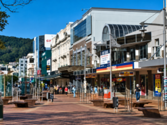 People walk along Courtenay Place in central Wellington, with shops, businesses and outdoor seating lining the street on a sunny day.