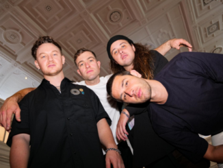 Members of Drax Project pose inside Wellington Town Hall, standing beneath the venue’s ornate restored ceiling ahead of the grand opening concert in February 2027.