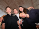 Members of Drax Project pose inside Wellington Town Hall, standing beneath the venue’s ornate restored ceiling ahead of the grand opening concert in February 2027.