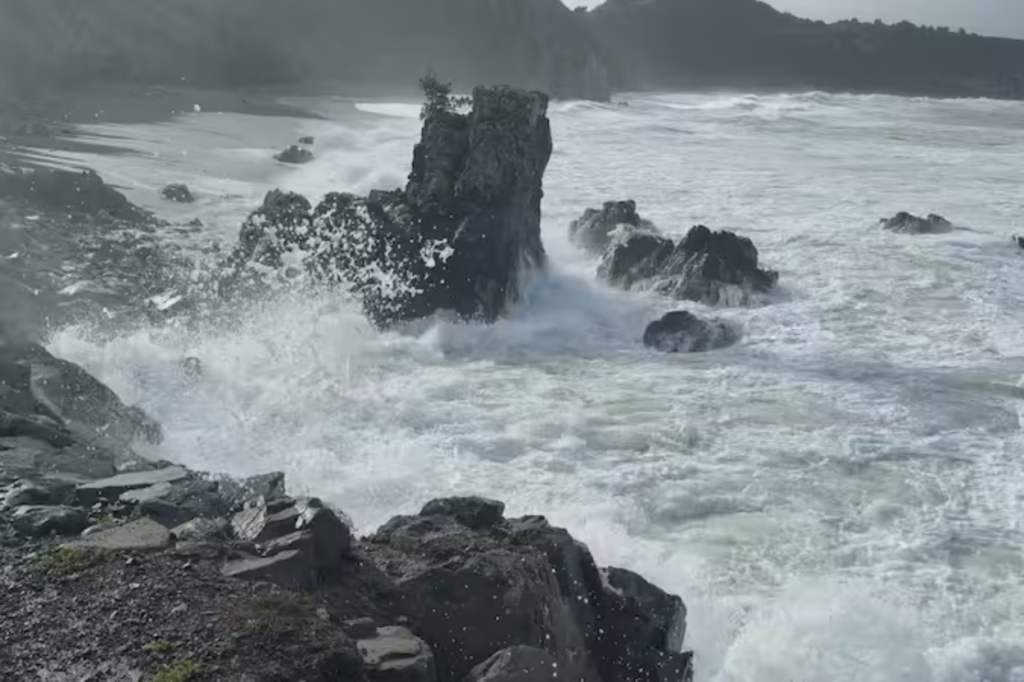 Large waves crash against rocks on a rugged Wellington region coastline during heavy swell conditions.