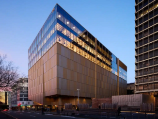 Te Rua Archives New Zealand building in Pipitea, Wellington, viewed at dusk. The large modern archive facility features a copper-toned lower façade and glass upper levels glowing with interior lights, with pedestrians and traffic visible along the street.