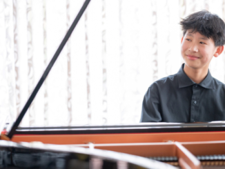 A teenage pianist seated at a grand piano, smiling and looking to the side
